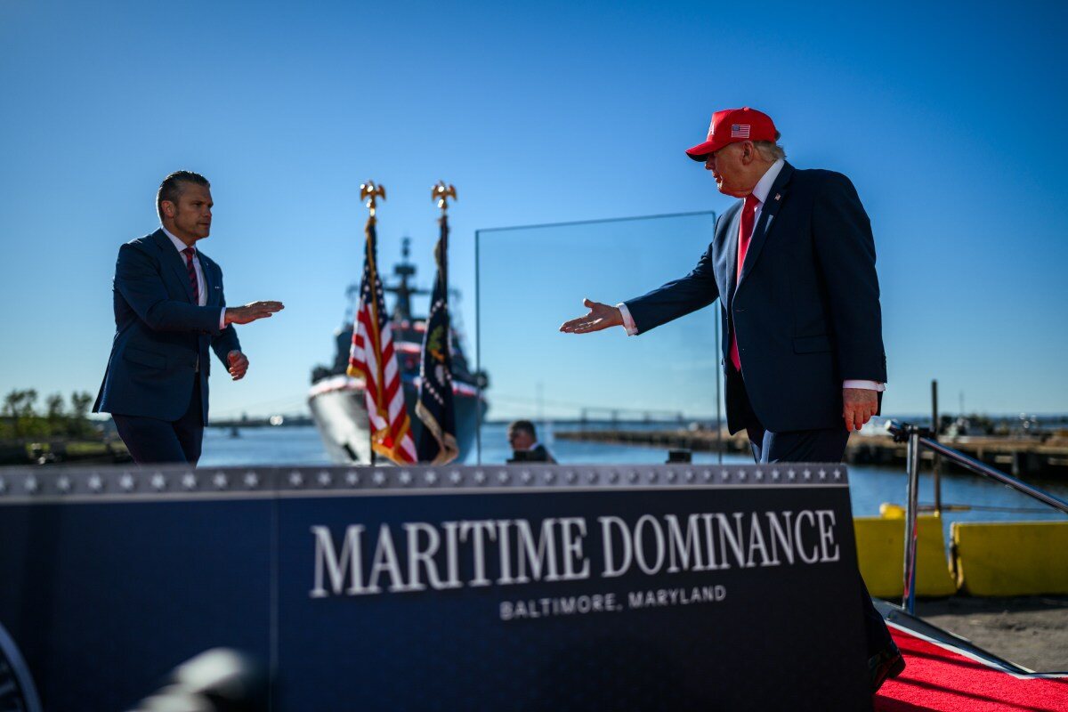 President Donald Trump stands on a waterfront stage marked Maritime Dominance, extending a hand toward another man.